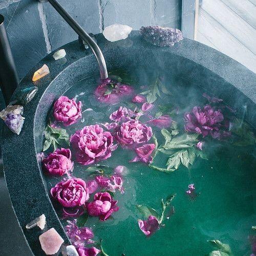 Uma banheira preparada para um ritual, com pétalas de flores, velas e cristais na borda.