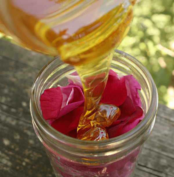 Um frasco com mel, um quartzo rosa e pétalas de rosa.